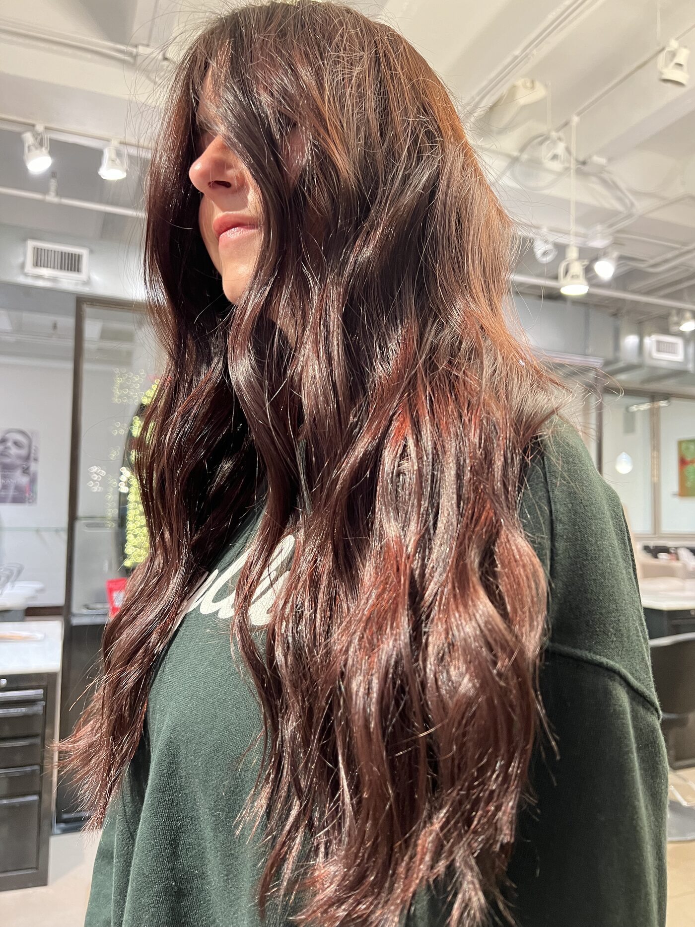Cherry cola hair color — a deep brown base with cherry-red tones showing through long waves, done at Red Market Miami