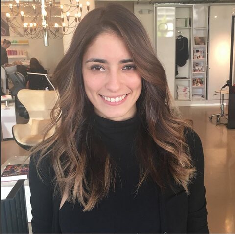 A smiling client with brown waves in the chairs beneath the chandelier at Red Market Miami